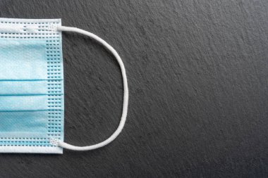 Koyu gri arka planda beyaz kulak lastiği bantlı tıbbi mavi maske. Koruyucu ekipmanın bir parçası. Kopyalama. Başlıklar ve tasarım için