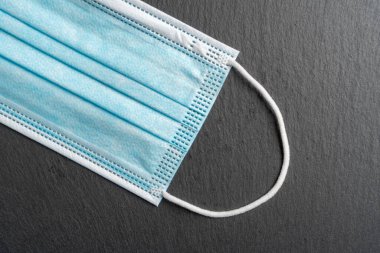 Yakın plan tıbbi tek kullanımlık maske. Koyu gri taştan bir arka planda koruyucu mavi maske. Renkli zıt görüş. Tıbbi koronavirüs konsepti