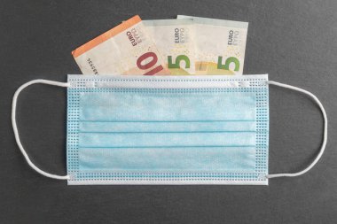 Yakın plan koruyucu tıbbi tek kullanımlık maske ve gri taşlı yüzeydeki euro banknotları. Ekonomik kriz sırasındaki iş kavramı