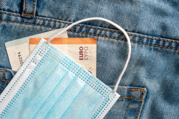 Euro banknotes and protective medical mask close-up on blue jeans. The idea of unemployment and the coronavirus pandemic