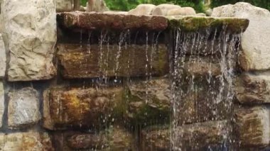 Yosunlu kahverengi taş duvar bir şelaleden gelen temiz su akıntılarıyla yıkanır. Yavaş çekim.