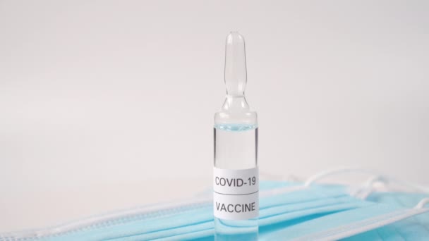 Szklana Ampułka Przezroczystym Płynem Nazwie Covid Vaccine Niebieskich Ochronnych Maskach — Wideo stockowe