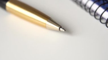 Altın renkli siyah kalem ve kapalı not defteri beyaz ofis masasında. İş ve eğitim için kişisel metal aksesuar