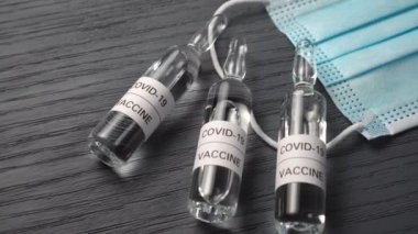 COVID-19 aşı kitini kapatın. Ampullerde Coronavirus aşısı ve gri ahşap bir masada tıbbi mavi maske. Küresel bir dünya virüsünün test ve üretimi kavramı