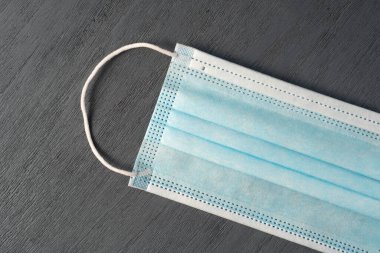 Gri ahşap arka planda lastik kulaklıklı cerrahi maske. Tipik 3 katlı cerrahi maske. Coronavirus koruma kavramı.