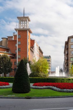 Oviedo, İspanya, Asturias - Ağustos 2020: Şehir meydanında yeşil çimenler ve Amerika Meydanı 'ndaki binaların arka planında parlak çiçekler bulunan çeşme