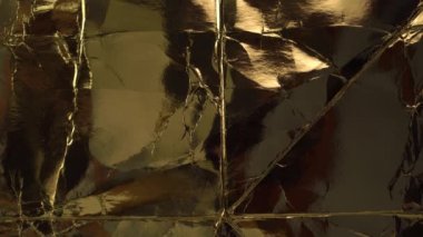 Altın kağıt dokusu, buruşuk eski, parlak ambalaj malzemesi. Işık hareketi