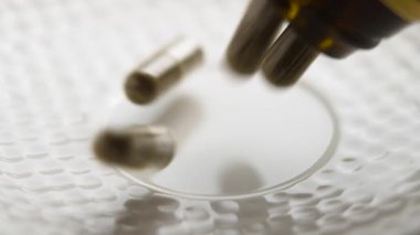 Beyaz seramik yüzeyde plastik şişeden yavaş çekimde düşen bitkisel ilaç kapsülleri. Alternatif ilaç hapları