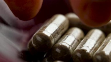 Parmaklar bitkisel toz özüyle dolu bir ilaç kapsülü alıyor. Makro