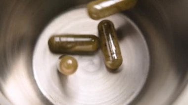 Bitkisel kapsüller metalik bir kabın içine dökülüyor. Şifa takviyeleri. Yavaş çekim