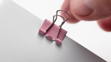 Eller, kağıt destesinden pembe metal bir ataç söküyor. Ofis işi kavramı