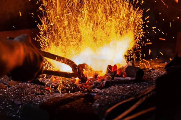 Manos irreconocibles de Smith preparando metal en yunque para forjar con fuegos artificiales de chispa Fotos De Stock