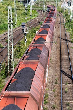 Uzun kömür treni kolonya içinde bir köprünün altından geçiyor.