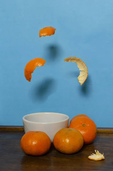 Mandalina ve peeling beyaz bir kase üzerinde düşüyor. Açık mavi arka plan. Hareket.
