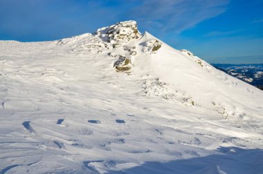 Karlı dağlar mavi bulutlu gökyüzünün altında görünür.