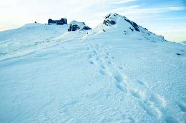 Karlı dağlar mavi bulutlu gökyüzünün altında görünür.