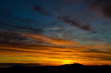 Karlı dağlar bulutlu günbatımı gökyüzünün altında görünür.