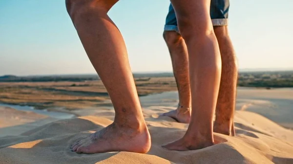 Santa Cruz, Bolivia - SEPT 5 2018: closeup of the legs of a young woman and man enjoying the sunset on the peak of one of the desert sand dune