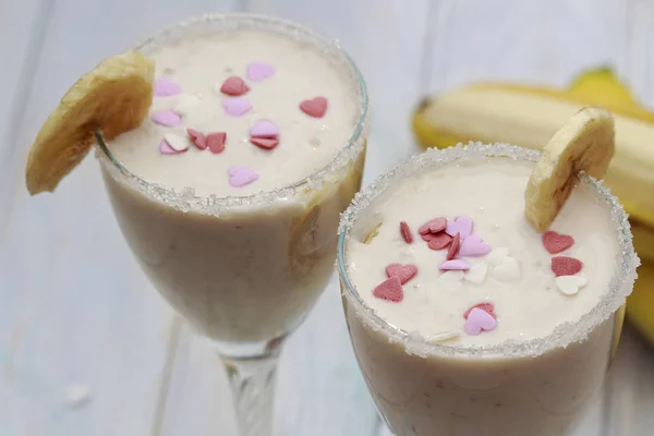Şeker kalpler ile dekore edilmiş muz parça ev yapımı muz smoothies ya da ahşap iki kadeh tabloda kokteylde süslenmiş