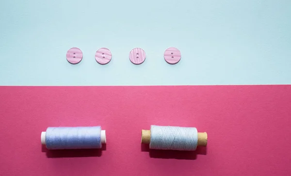 Composition with blue threads and sewing accessories on pink background. Pink buttons on blue background. Flatlay, place for text — Stock Photo, Image