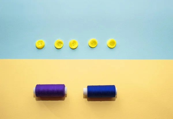 Composition with dark blue threads and sewing accessories on yellow background. Yellow buttons on blue background. Flatlay, place for text — Stock Photo, Image