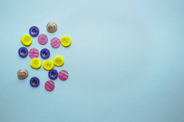 mavi arka plan üzerinde çeşitli çok renkli dikiş düğmesi koleksiyonu. Sarı, mor, lacivert düğmeler. Minimalizm. Dikiş aksesuarları. Flatlay, metin yeri