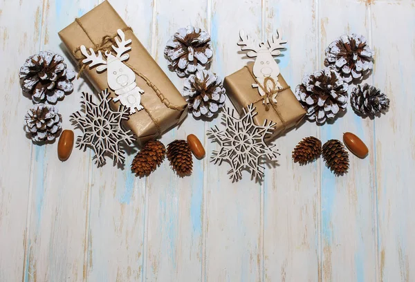 Christmas holidays composition on white wooden background. Craft boxes of gifts, wooden deer and snowflakes, fir cones, pine cones. Concept of happy (marry) christmas card.