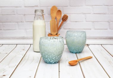 Kefir, süt, mavi bardakta yoğurt. Mutfak ahşap kaşıkları beyaz bir duvarın arkasında.