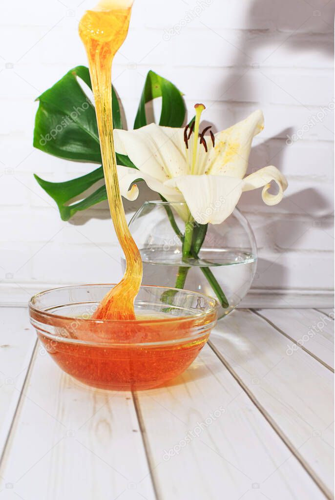 Liquid sugar paste for hair removal in a bowl with lily flower and dracaena leaf in glass vase. The concept of body care, beauty treatments.