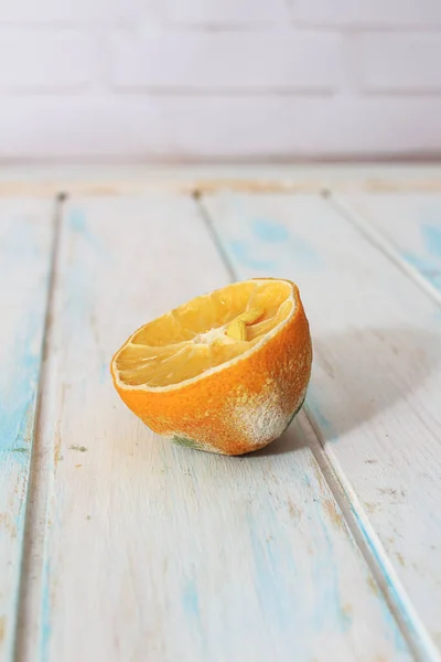 Half a rotten lemon. Lemon with green and white mold on white wooden background