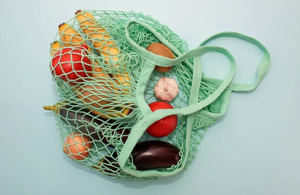 Cotton string bag with vegetables tomatoes, eggplant, onion, garlic on blue background. Eco-friendly shopping without plastic