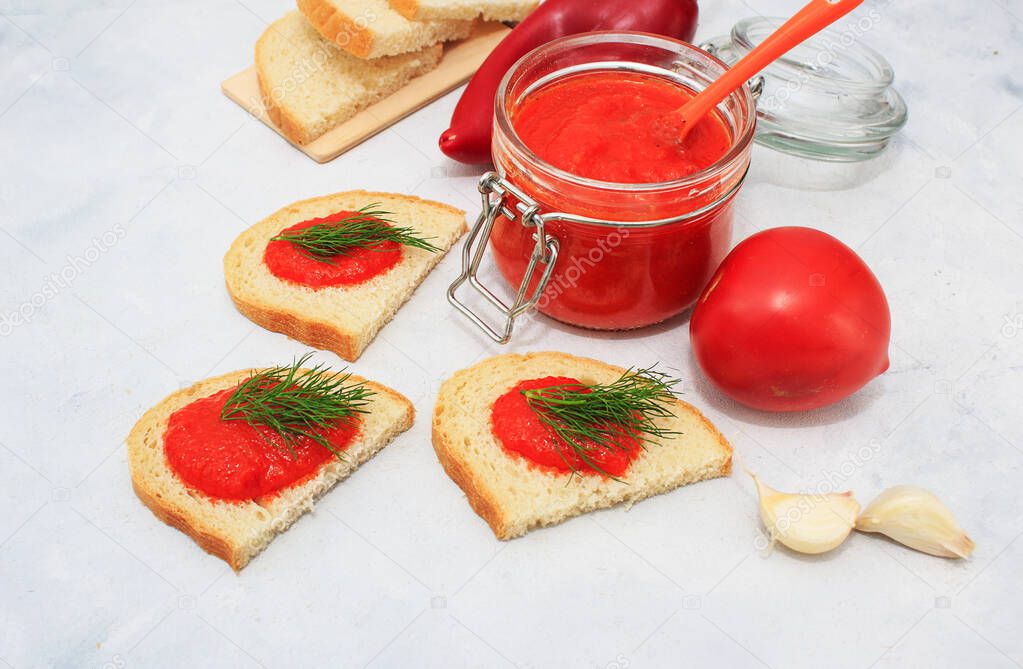 Ajvar, pepper mousse in a jar and on bread and gray backgground. Ajvar - delicious dish of red peppers, tomato and garlic.