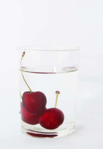 Cerezas frescas cayendo en un vaso de agua con burbujas sobre un fondo blanco. — Foto de Stock