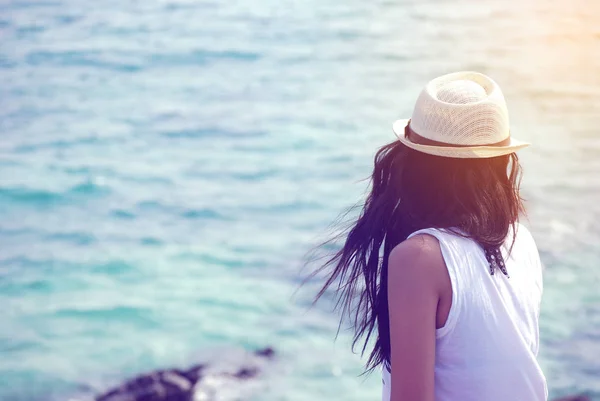 Long hair woman wearing a hat, sitting lonely looking at the sea.