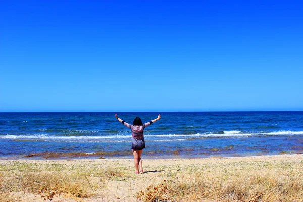 A girl stands on the beach and pulls hands to the sky on a sunny day