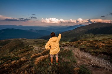 Sarı yağmurluk bir dağın tepesinde bir genç adam. Karpatlar, Ukrayna