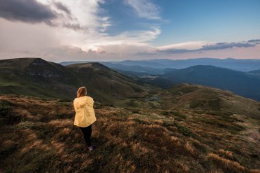 A young woman in a yellow raincoat on top of a mountain. Carpathians, Ukraine clipart