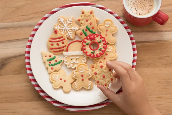Christmas time: person taking Gingerbread Christmas cookies and a mug with milk and cinnamon on wooden board