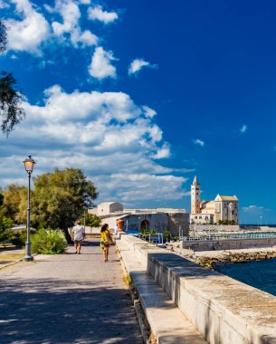 İki sevgili el ele tutuşarak, Trani belediye parkında deniz manzarası ve arka planda Aziz Nicholas Pilgrim Katedral Bazilikası ile yürüyor. Puglia 'da, Bari yakınlarında, Barletta, Andria.