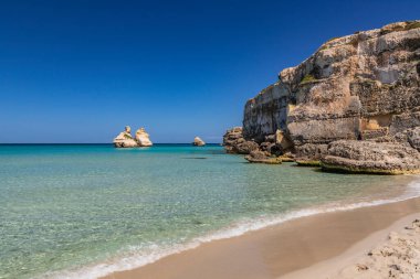 Torre dell 'Orso körfezi, yüksek uçurumları, Salento, Puglia, İtalya. Turkuaz deniz ve mavi gökyüzü, yazın güneşli bir gün. Güzel beyaz ve pembe kumdan oluşan bir kumsal. Yığınların adı İki Kız Kardeş..