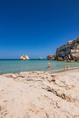 Torre dell 'Orso körfezi, yüksek uçurumlarıyla, Salento, Puglia' da. Güzel beyaz kumsal. Yığınlar İki Kız Kardeş 'i çağırdı. Güzel kız köpeğiyle turkuaz denizde banyo yapıyor ve oynuyor.