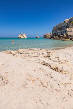Torre dell 'Orso körfezi, yüksek uçurumlarıyla, Salento, Puglia' da. Güzel beyaz kumsal. Yığınlar İki Kız Kardeş 'i çağırdı. Güzel kız köpeğiyle turkuaz denizde banyo yapıyor ve oynuyor.