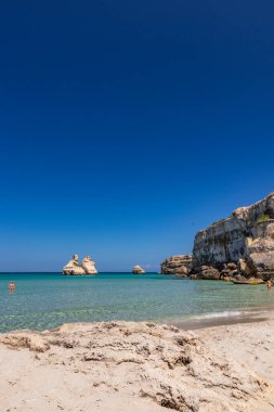 Torre dell 'Orso körfezi, yüksek uçurumları, Salento, Puglia, İtalya. Turkuaz deniz ve mavi gökyüzü. Güzel beyaz kumsal. Yığınlar İki Kız Kardeş 'i çağırdı. Denizde yıkanan güzel kız.