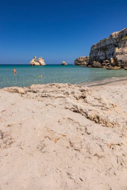 Torre dell 'Orso körfezi, yüksek uçurumlarıyla, Salento, Puglia' da. Güzel beyaz kumsal. Yığınlar İki Kız Kardeş 'i çağırdı. Güzel kız köpeğiyle turkuaz denizde banyo yapıyor ve oynuyor.