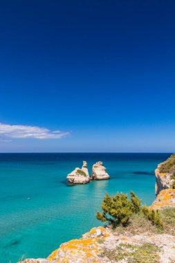 Torre dell 'Orso körfezi, yüksek uçurumları, Salento, Puglia, İtalya. Turkuaz deniz ve mavi gökyüzü, yazın güneşli bir gün. Yığınlar İki Kız Kardeş 'i çağırdı. Bir insan berrak suda yüzer.