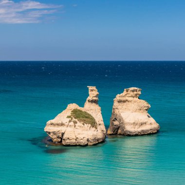 Torre dell 'Orso körfezi, yüksek uçurumları, Salento, Puglia, İtalya. Turkuaz deniz ve mavi gökyüzü, yazın güneşli bir gün. Yığınlar İki Kız Kardeş 'i çağırdı. Bir insan berrak suda yüzer.