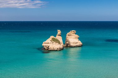 Torre dell 'Orso körfezi, yüksek uçurumları, Salento, Puglia, İtalya. Turkuaz deniz ve mavi gökyüzü, yazın güneşli bir gün. Yığınlar İki Kız Kardeş 'i çağırdı. Bir insan berrak suda yüzer.