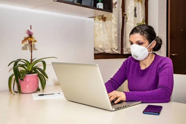 Corona Virus, Covid-19. Stay at home. Quarantine. Protection mask. A beautiful Caucasian woman forced to stay home to prevent virus infection, works on the laptop. Smart Working.