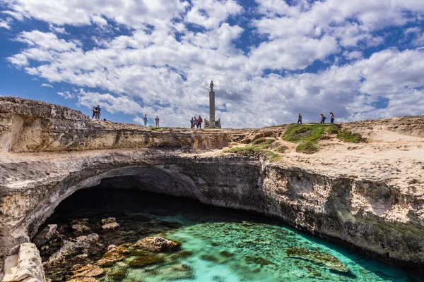 Archaeological site and tourist resort of Roca Vecchia, Puglia, Salento, Italy. Turquoise sea, clear blue sky, rocks, sun, in summer. The Cave of Poetry. Tourists take pictures and sunbathe.