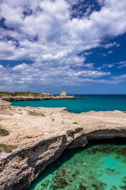 Roca Vecchia, Puglia, Salento, İtalya 'da arkeolojik alan ve turizm beldesi. Turkuaz deniz, berrak mavi gökyüzü, kayalar, güneş, yazın. Şiir Mağarası. Arka plandaki gözetleme kulesi..